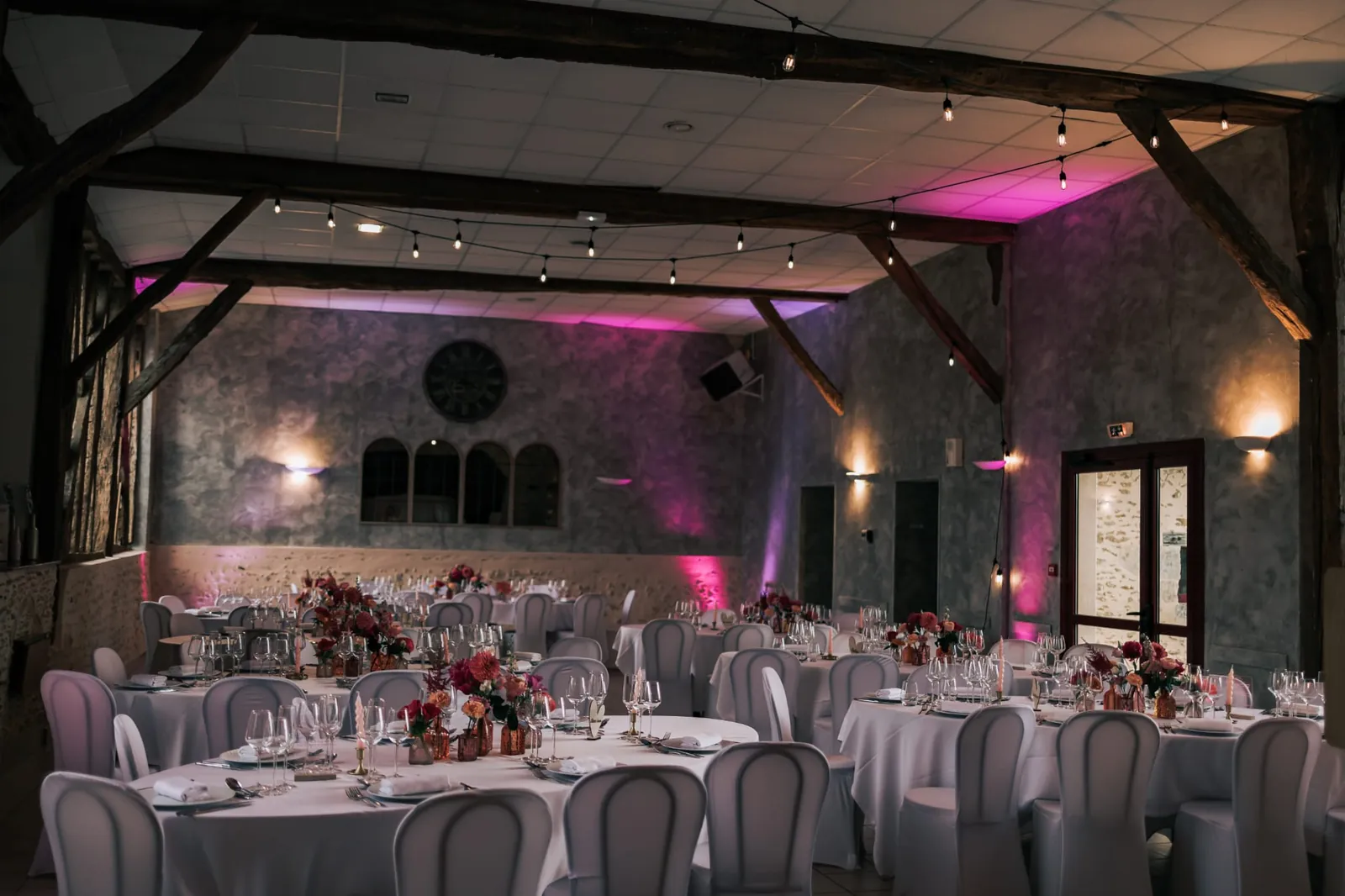 La salle de réception illuminée de rose, tables rondes dressées