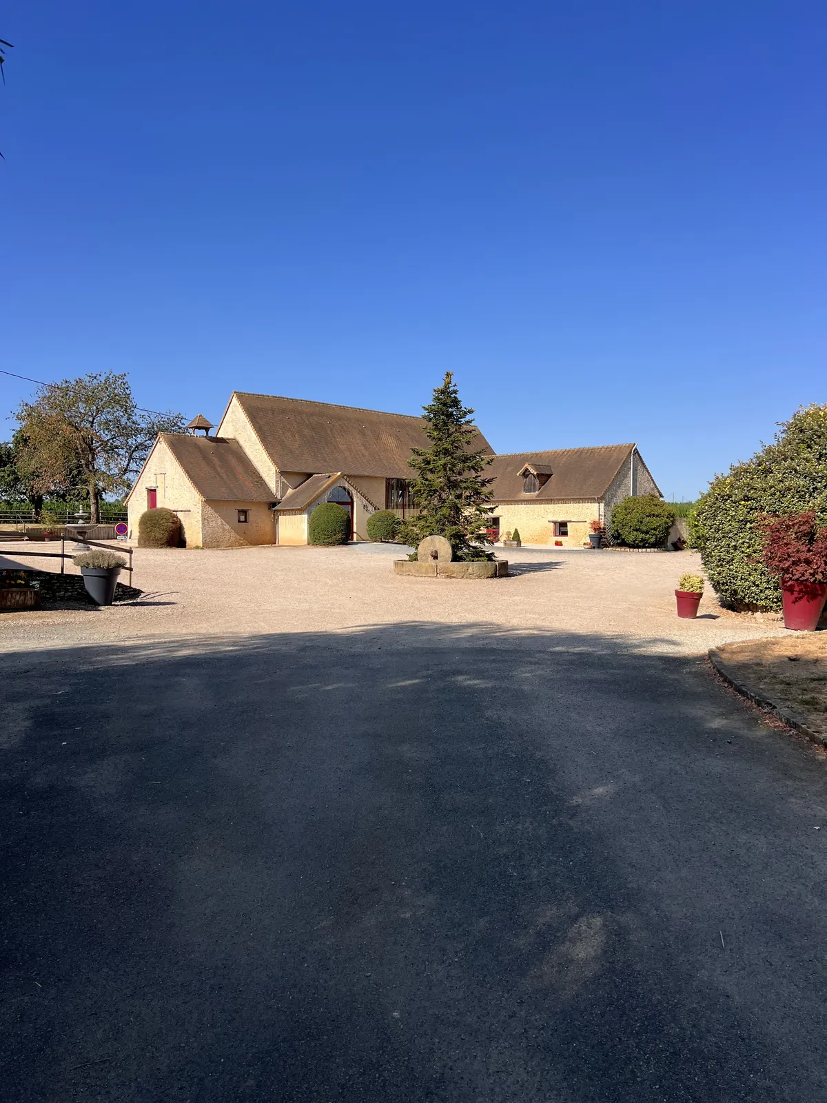 L’allée d’arrivée vers les bâtiments en pierre du domaine, sous un ciel bleu