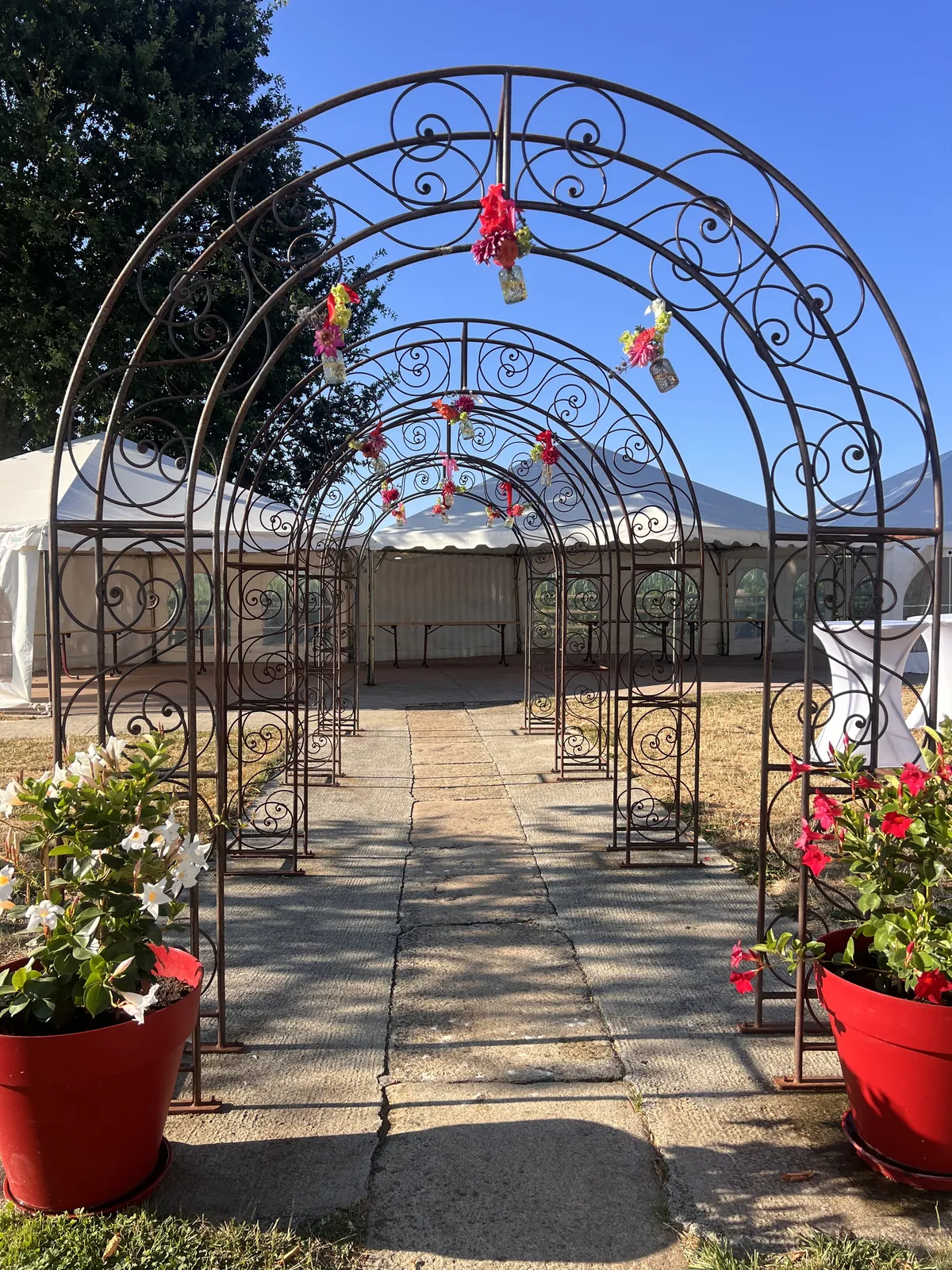 L’allée d’arches en fer forgé, fleurie, vers les barnums