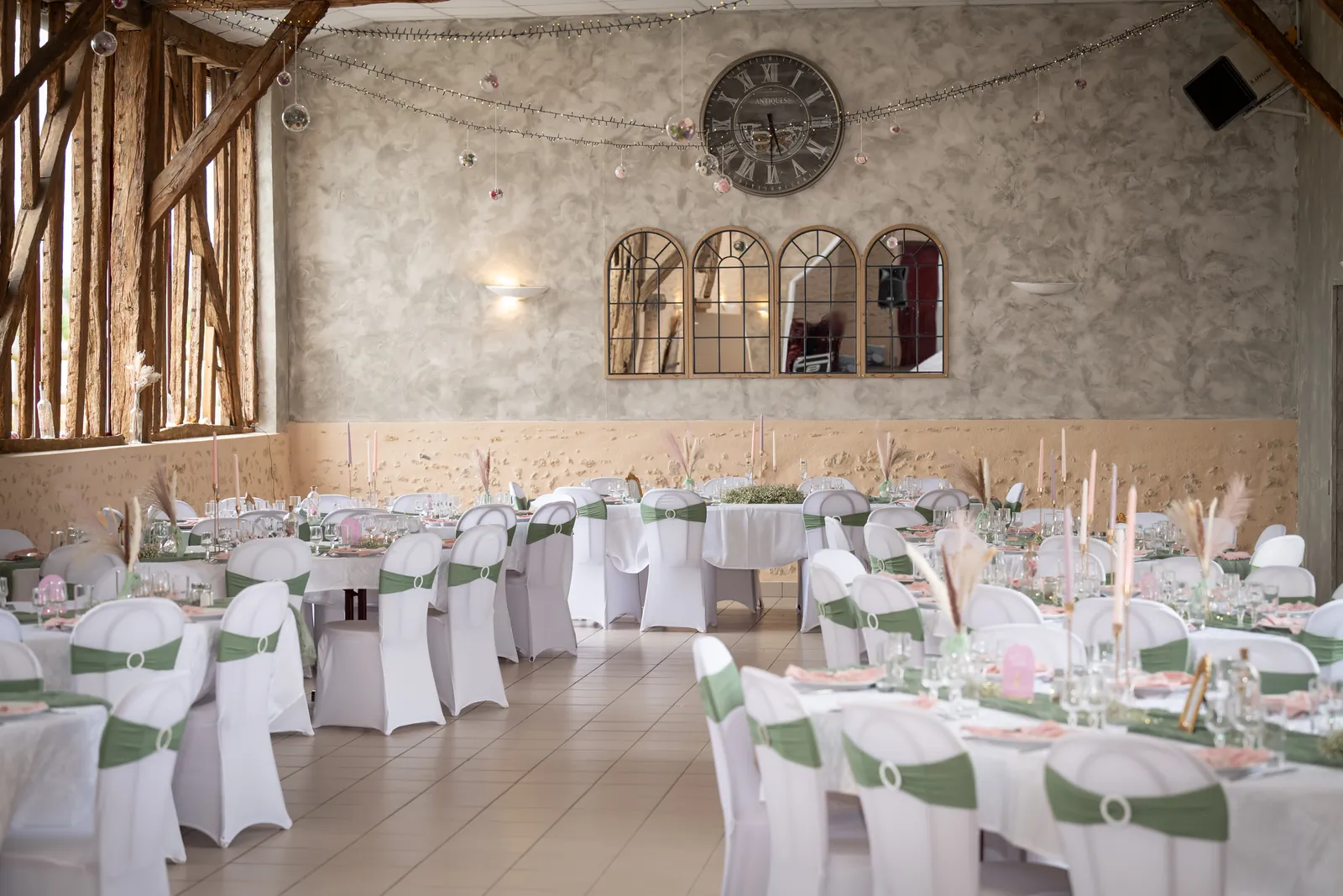 La salle en tables rondes, housses blanches et nœuds verts, sous l’horloge